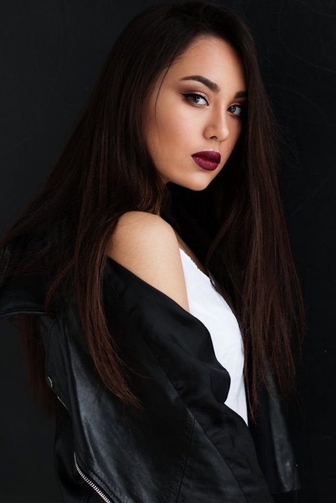 Elegant portrait of a young woman with striking makeup, posing in a black leather jacket.